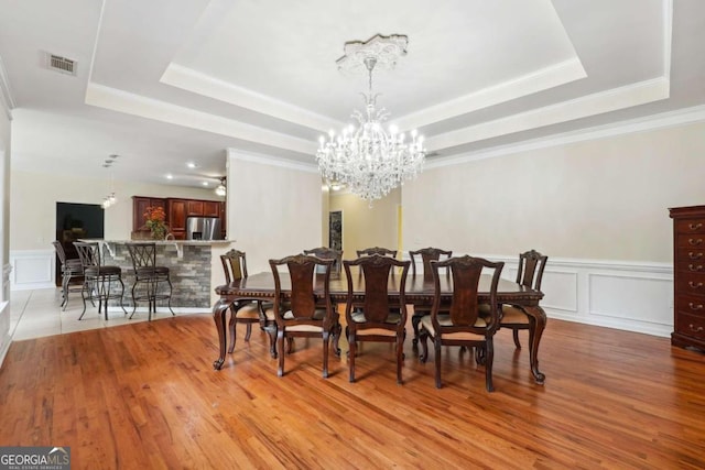 dining room with light hardwood / wood-style floors, a notable chandelier, a tray ceiling, and ornamental molding