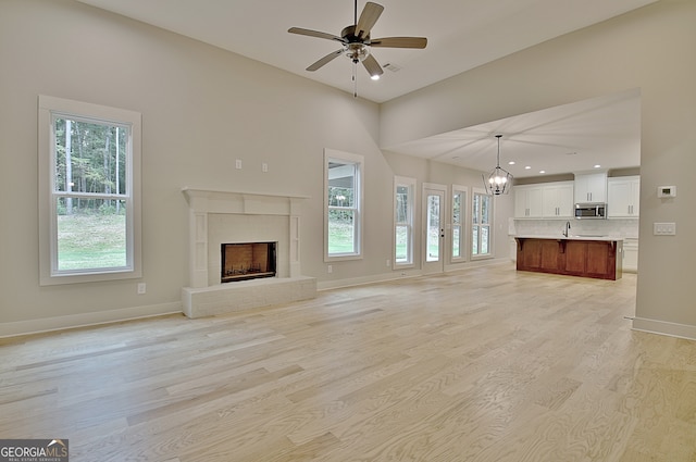 unfurnished living room featuring ceiling fan with notable chandelier, light wood-type flooring, and a healthy amount of sunlight