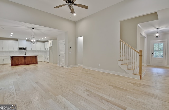 unfurnished living room with ceiling fan with notable chandelier, light wood-type flooring, and sink