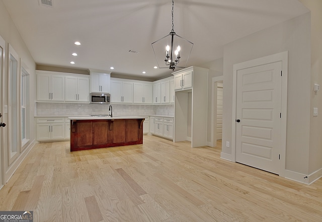 kitchen with a chandelier, a center island with sink, light hardwood / wood-style floors, and backsplash