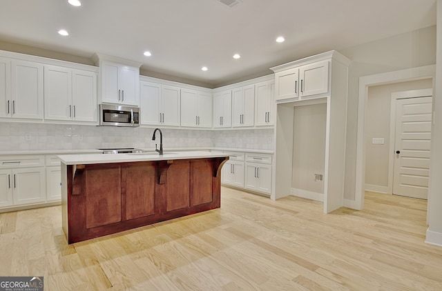 kitchen featuring light hardwood / wood-style floors, an island with sink, white cabinets, backsplash, and sink