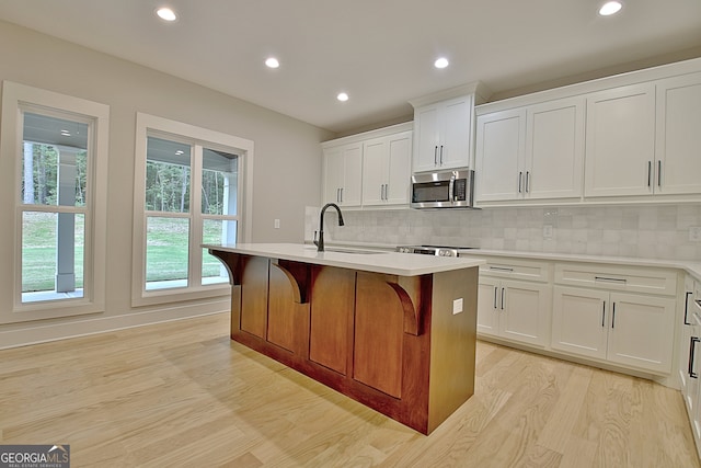 kitchen with an island with sink, light wood-type flooring, sink, and a wealth of natural light