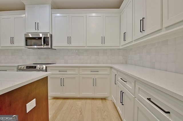 kitchen with light hardwood / wood-style floors, light stone counters, tasteful backsplash, white cabinets, and stainless steel appliances