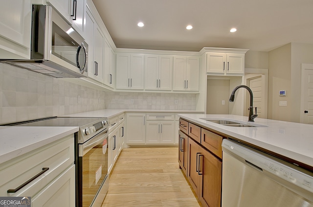 kitchen with appliances with stainless steel finishes, light wood-type flooring, sink, and white cabinetry