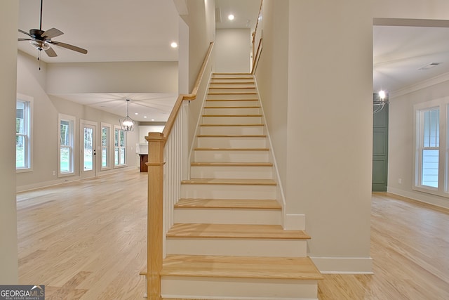 stairs with ceiling fan with notable chandelier, ornamental molding, and hardwood / wood-style flooring