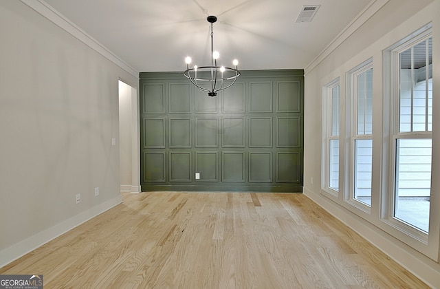 unfurnished dining area featuring light wood-type flooring, ornamental molding, and an inviting chandelier