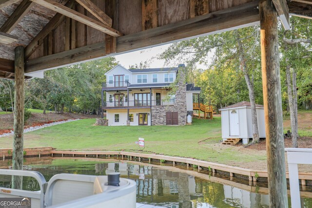 rear view of property with a storage unit, a lawn, a water view, and a balcony