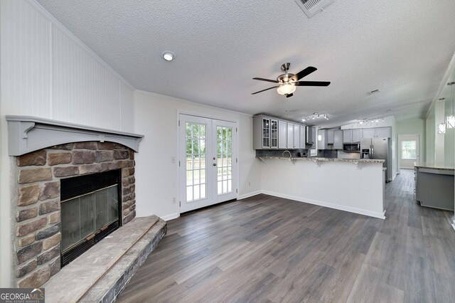 unfurnished living room with hardwood / wood-style floors, a stone fireplace, a textured ceiling, ceiling fan, and crown molding