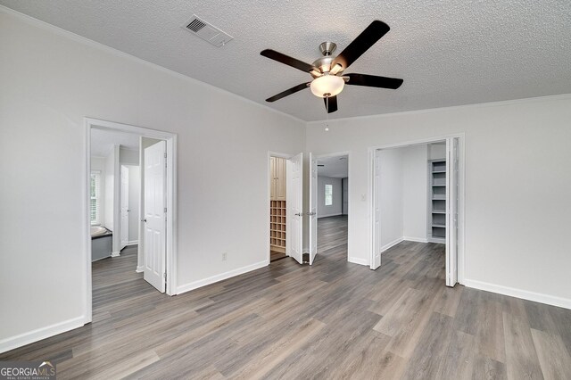 unfurnished bedroom with ensuite bath, hardwood / wood-style flooring, a spacious closet, a textured ceiling, and ceiling fan