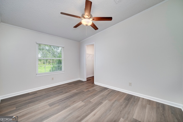 spare room featuring wood-type flooring, vaulted ceiling, a textured ceiling, ceiling fan, and crown molding