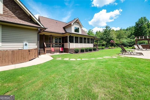 back of property with a shingled roof, fence, a lawn, a sunroom, and a patio