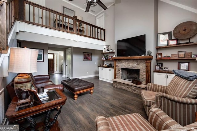 living room featuring a towering ceiling, ceiling fan, dark hardwood / wood-style floors, and a stone fireplace