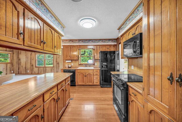 kitchen featuring a textured ceiling, a healthy amount of sunlight, black appliances, and wood walls