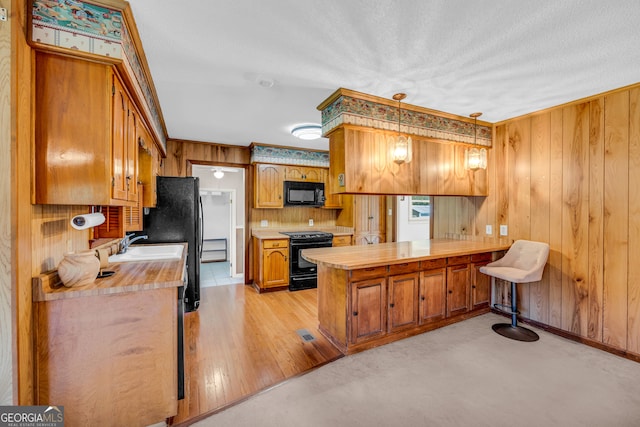 kitchen featuring wood walls, black appliances, hanging light fixtures, light hardwood / wood-style floors, and kitchen peninsula