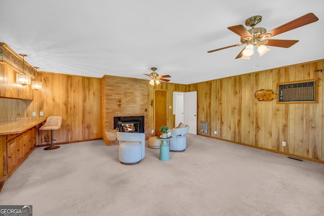 living room featuring light carpet, a large fireplace, ceiling fan, and wooden walls