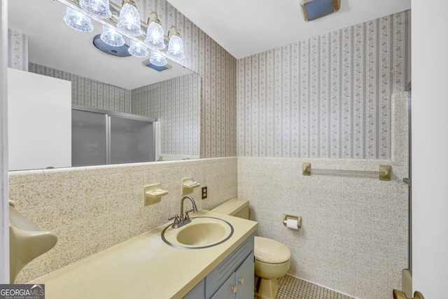 bathroom featuring tile patterned flooring, toilet, a shower with door, vanity, and tile walls