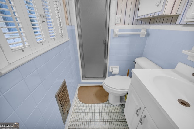 bathroom with vanity, a shower with door, tile patterned floors, toilet, and tile walls