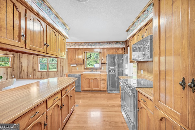 kitchen with a wealth of natural light, wooden walls, black appliances, and light wood-type flooring