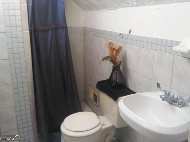 bathroom featuring sink, curtained shower, tile walls, and toilet