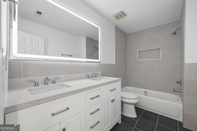 full bathroom with toilet, double vanity, tile walls, tile patterned floors, and tiled shower / bath combo