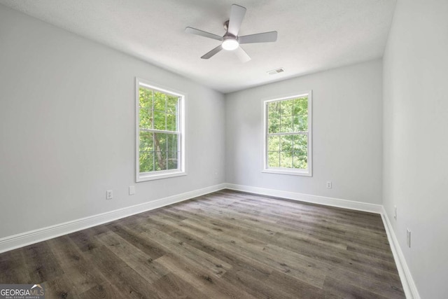 empty room with ceiling fan, plenty of natural light, and dark wood-type flooring