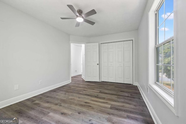 unfurnished bedroom with ceiling fan, a closet, dark hardwood / wood-style flooring, and multiple windows