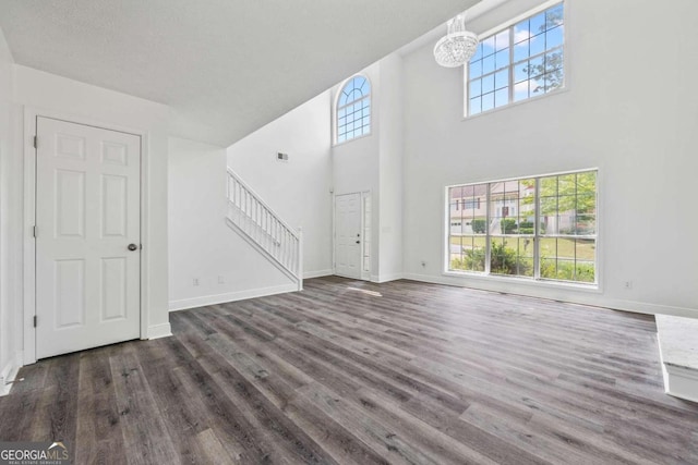 unfurnished living room featuring an inviting chandelier, dark wood-type flooring, and a high ceiling