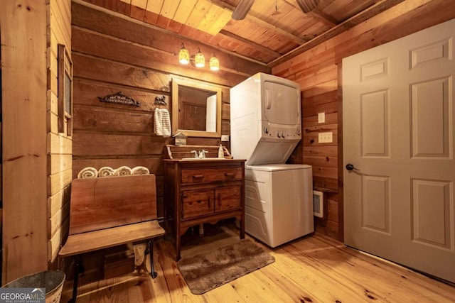 washroom featuring wooden walls, stacked washer / drying machine, light hardwood / wood-style floors, wooden ceiling, and sink