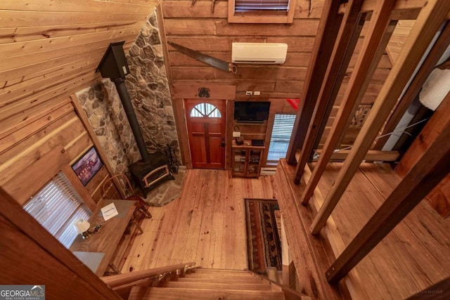 living room with wood-type flooring, a wood stove, wooden walls, and a wall unit AC