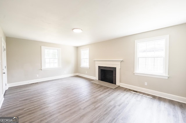 unfurnished living room featuring a brick fireplace, wood finished floors, visible vents, and baseboards