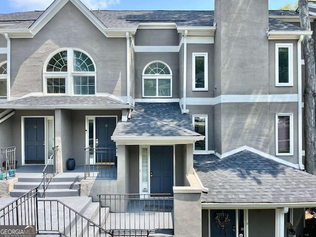 townhome / multi-family property featuring roof with shingles, a chimney, and stucco siding