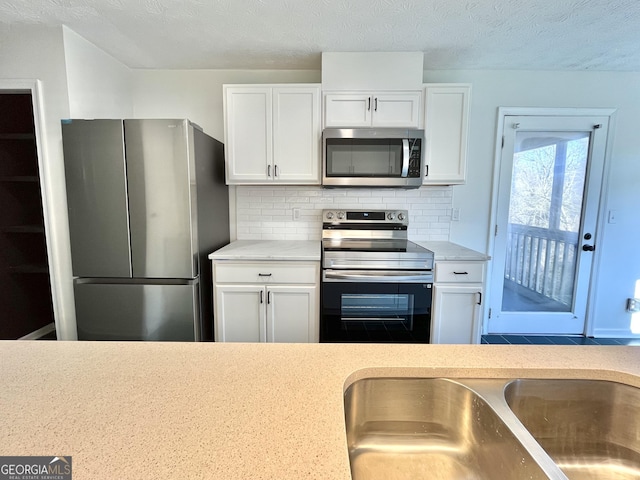 kitchen featuring a textured ceiling, appliances with stainless steel finishes, backsplash, and white cabinets