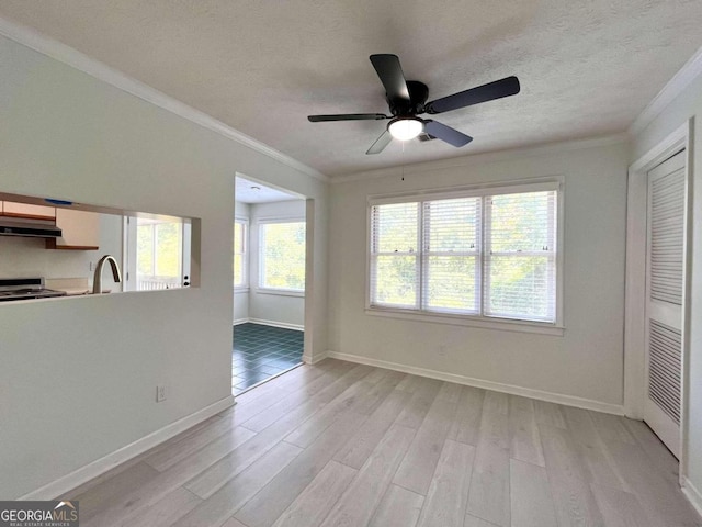 unfurnished living room with a textured ceiling, a sink, baseboards, ornamental molding, and light wood-type flooring