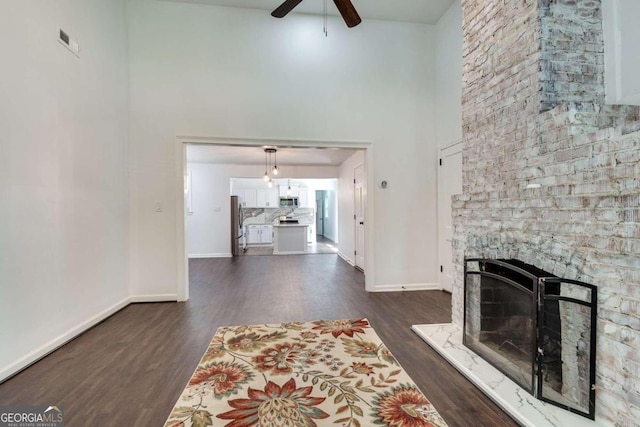 living room featuring ceiling fan, dark hardwood / wood-style floors, a large fireplace, and a towering ceiling