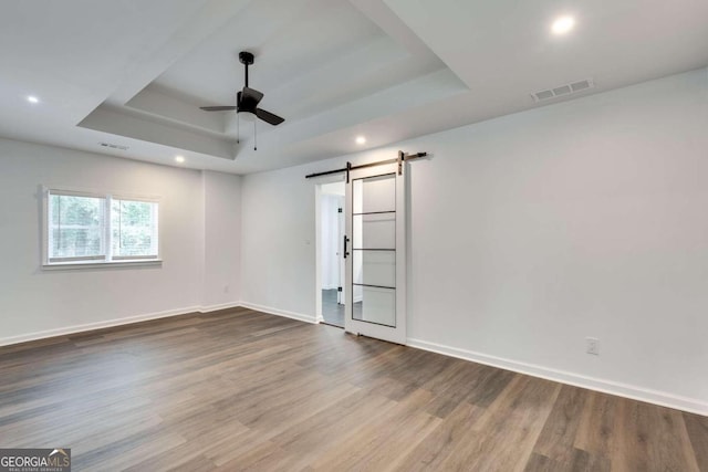 unfurnished room with ceiling fan, a raised ceiling, wood-type flooring, and a barn door