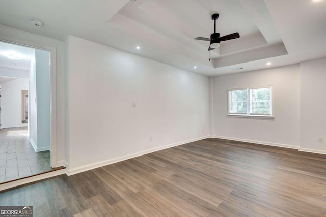 empty room with hardwood / wood-style flooring, a raised ceiling, and ceiling fan