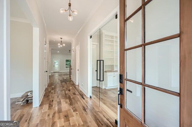 corridor with light wood-type flooring and an inviting chandelier