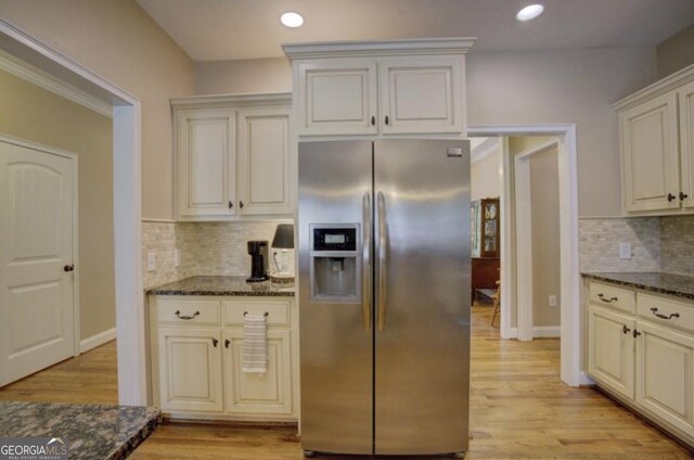 kitchen with light wood-type flooring, backsplash, dark stone countertops, and stainless steel fridge with ice dispenser