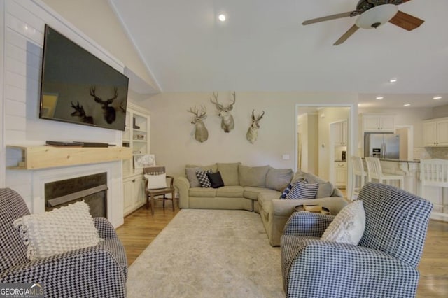 living room with light hardwood / wood-style flooring, ceiling fan, and vaulted ceiling
