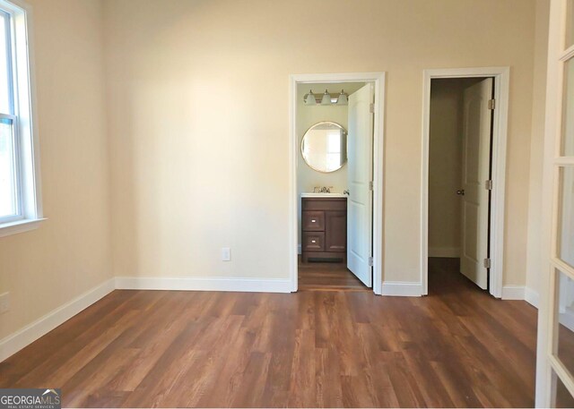 unfurnished bedroom featuring dark hardwood / wood-style floors, sink, and ensuite bathroom