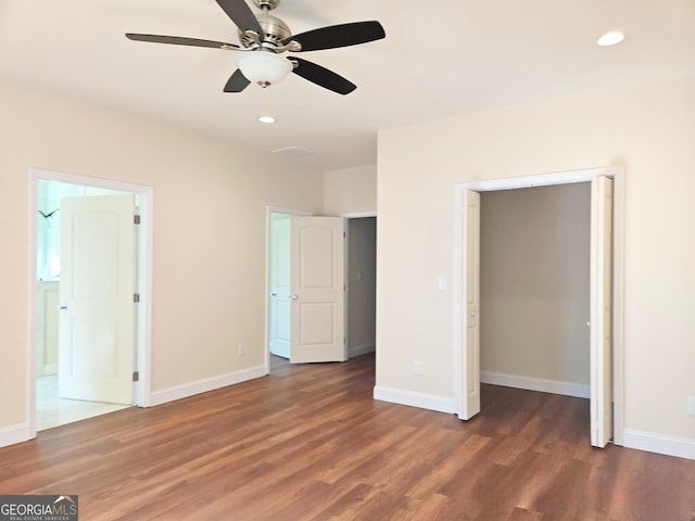 unfurnished bedroom with a spacious closet, baseboards, recessed lighting, ensuite bathroom, and wood finished floors