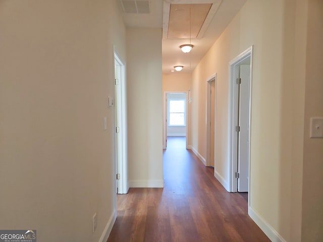 hallway with attic access, baseboards, visible vents, and dark wood-style flooring