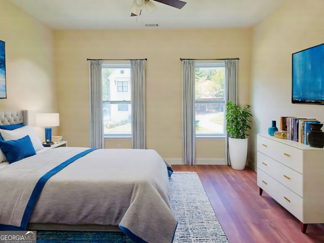 bedroom featuring visible vents, a ceiling fan, baseboards, and wood finished floors