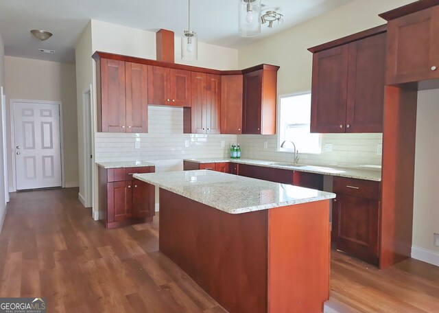 kitchen featuring a center island, light stone counters, dark hardwood / wood-style flooring, sink, and decorative backsplash