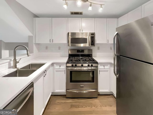 kitchen featuring white cabinets, rail lighting, light hardwood / wood-style flooring, and stainless steel appliances