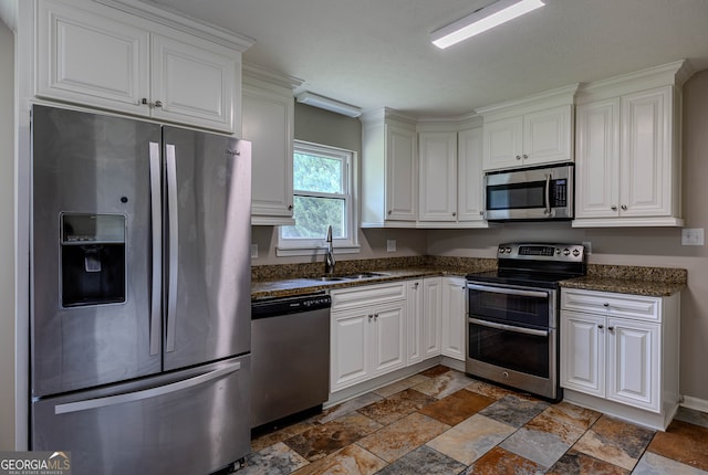 kitchen featuring stainless steel appliances, dark tile patterned floors, sink, white cabinets, and dark stone counters