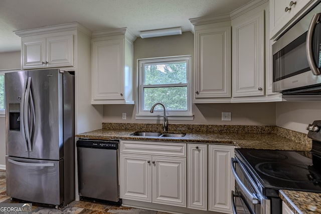 kitchen featuring appliances with stainless steel finishes, sink, dark stone countertops, and white cabinets