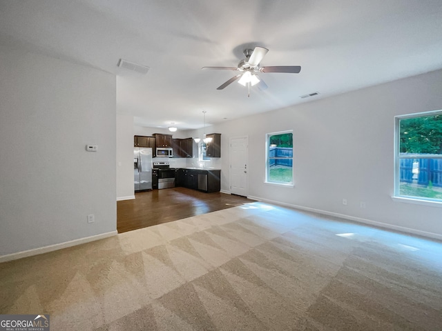 unfurnished living room with ceiling fan, dark carpet, visible vents, and baseboards