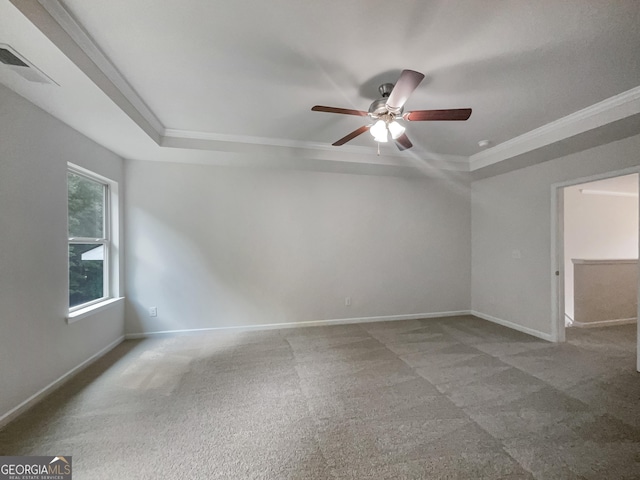 carpeted spare room with visible vents, a ceiling fan, baseboards, ornamental molding, and a raised ceiling