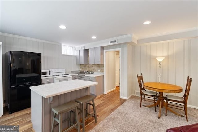 kitchen with decorative backsplash, gray cabinets, a kitchen bar, light hardwood / wood-style floors, and white appliances